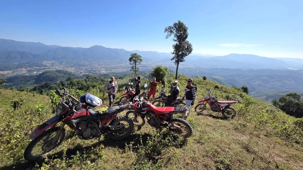 Dirt bike riders and motorcycles at a mountain viewpoint in northern Laos