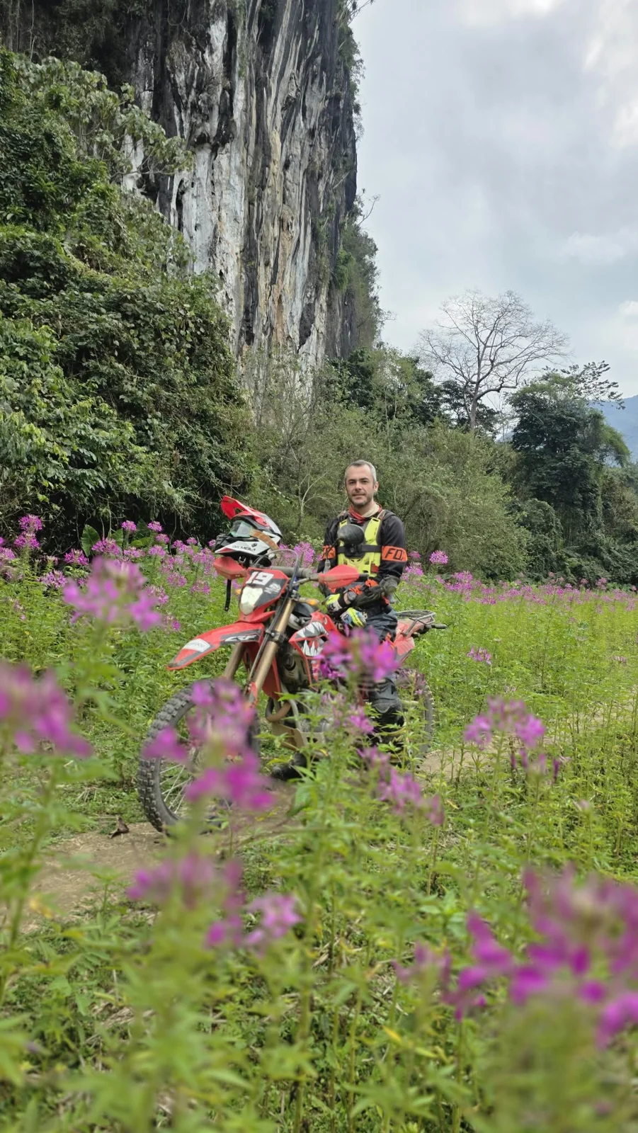 A rider and motorcycle beneath limestone cliffs.