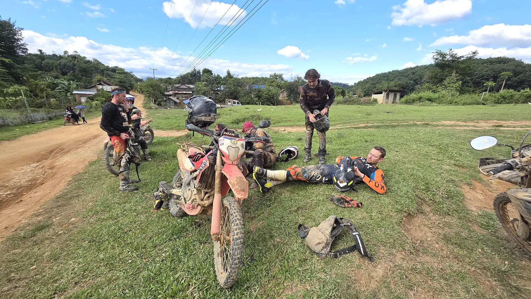 Riders checking a dirt bike beside a remote trail in Laos